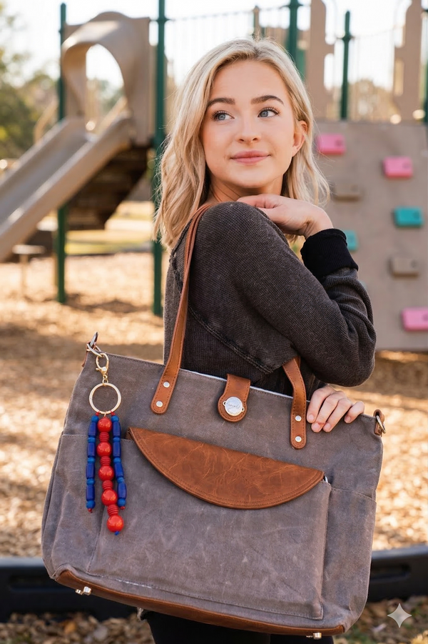 Woman holding a gray tote bag with brown accents at a playground.