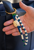Hand holding a beaded keychain with blue and white beads against a dark background