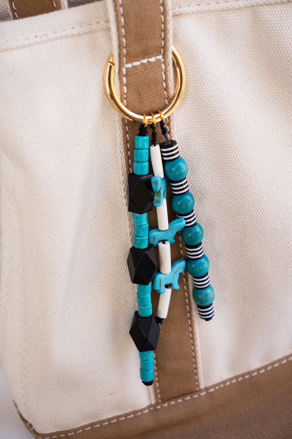 Close-up of a beaded keychain attached to a bag strap with a beige background.