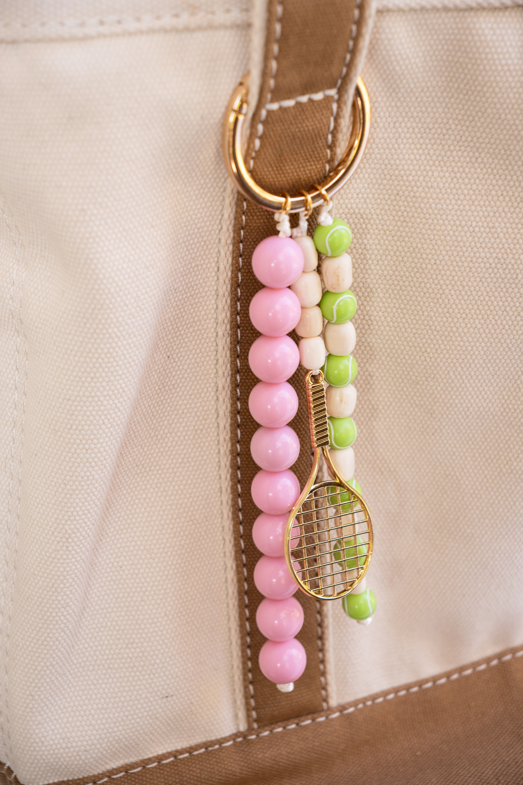 Beaded keychain with pink, green, and gold elements attached to a beige bag.