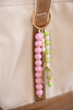 Beaded keychain with pink, green, and gold elements attached to a beige bag.
