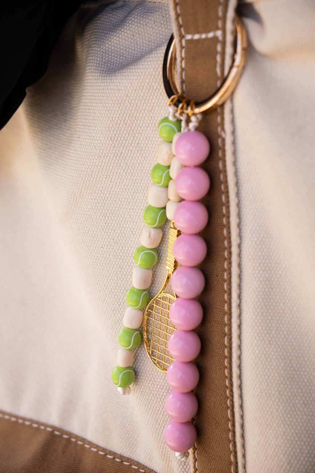 Beaded keychain with pink and green beads attached to a beige jacket.
