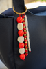 Black handbag with a decorative bead strap featuring red, white, and gold beads.