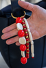 Hand holding a keychain with red, white, and gold beads against a blurred background