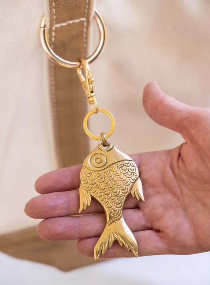 Gold fish-shaped keychain held in a hand with a neutral background
