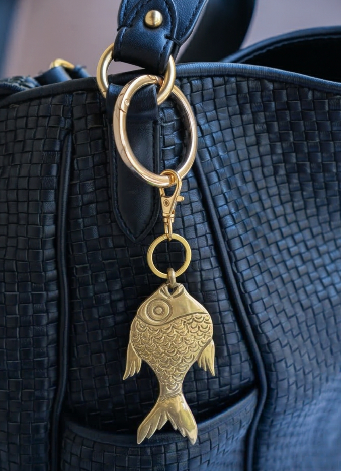 Brass fish-shaped keychain attached to a black textured bag.