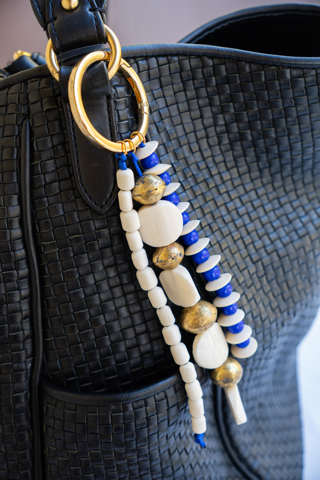 Beaded handbag strap with blue, white, and gold beads on a black textured bag.