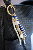 Beaded handbag strap with blue, white, and gold beads on a black textured bag.