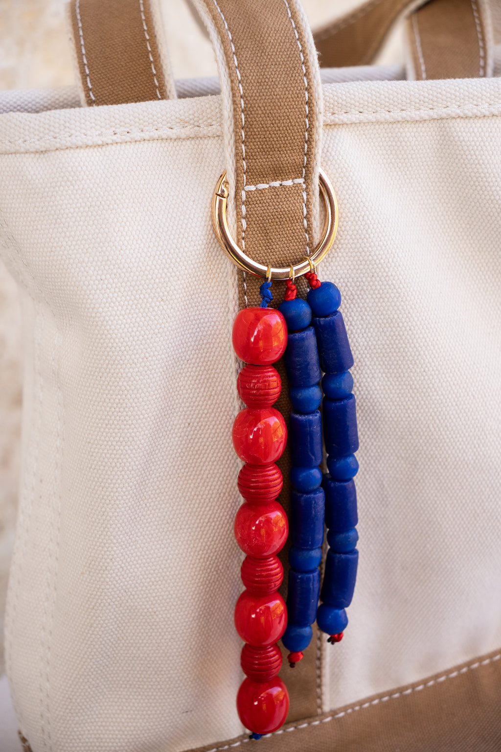 Beaded keychain with red and blue beads attached to a beige bag.