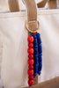 Beaded keychain with red and blue beads attached to a beige bag.