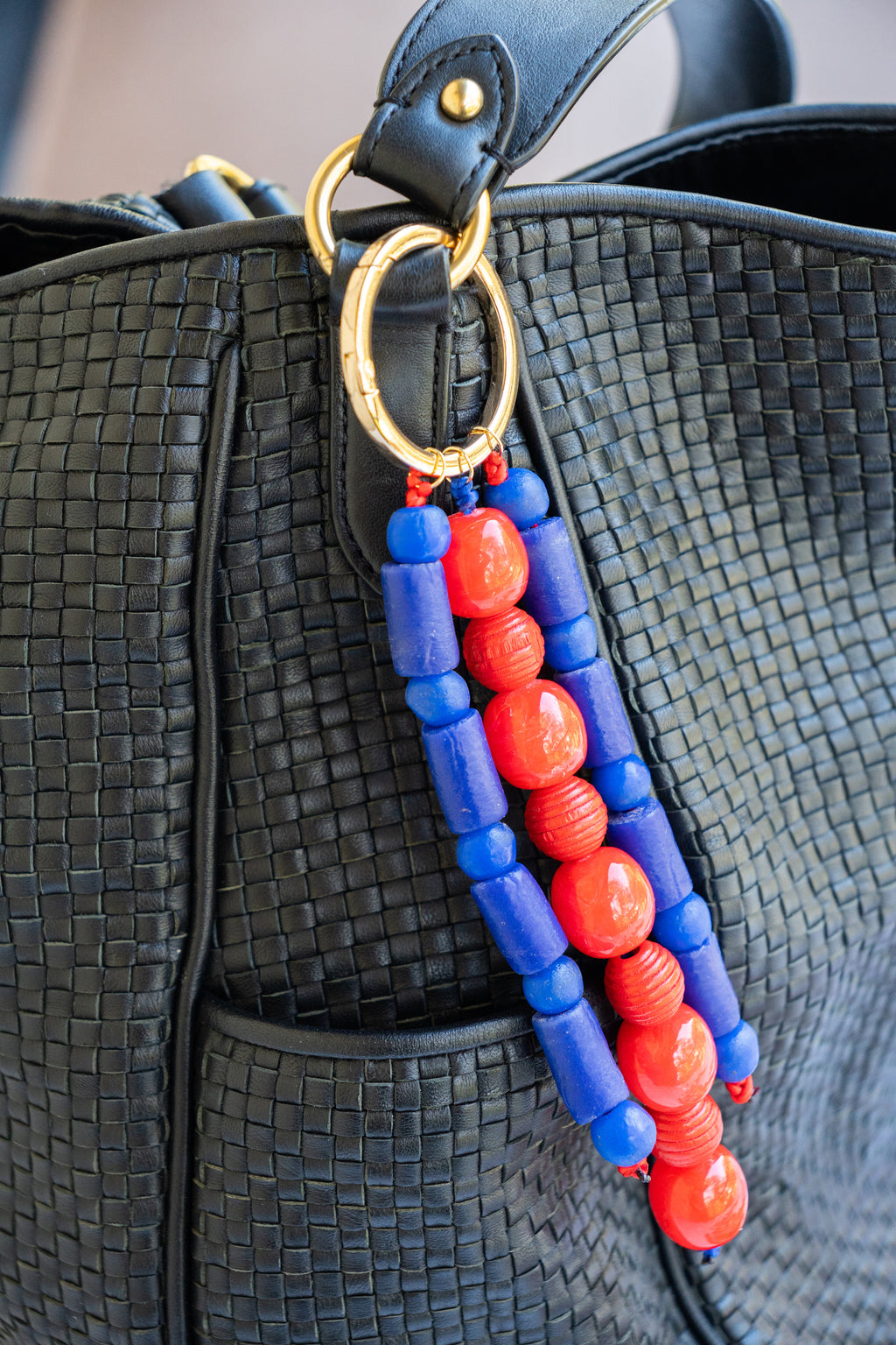 Black textured handbag with a beaded strap featuring blue and red beads.