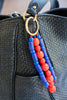 Black textured handbag with a beaded strap featuring blue and red beads.
