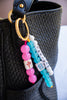 Colorful beaded keychain with 'Mahjong' text attached to a black woven bag.