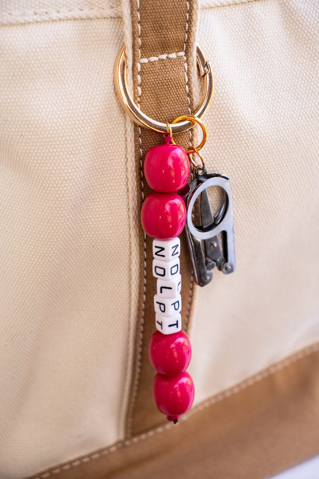 Bag Charm with red beads and a carabiner attached to a beige bag.