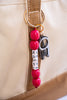 Bag Charm with red beads and a carabiner attached to a beige bag.