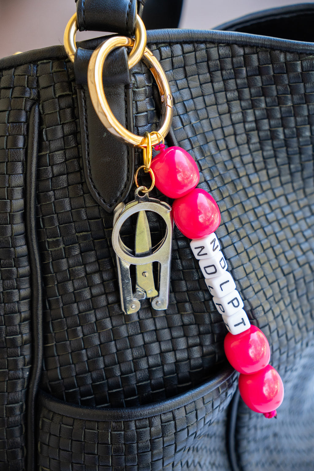 Bag Charm with pink beads and gold chain attached to a black textured bag.