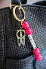 Bag Charm with pink beads and gold chain attached to a black textured bag.