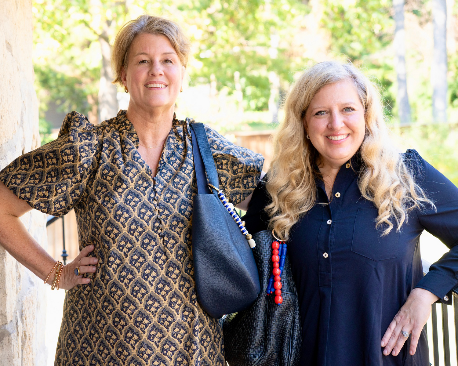 Two women standing outdoors, one holding a blue handbag.